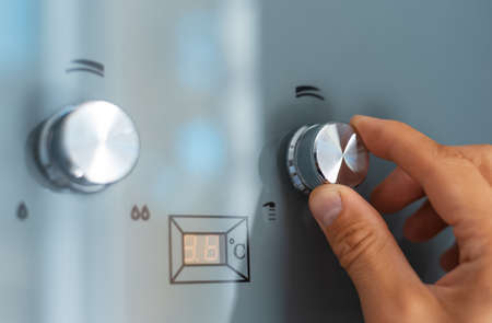 Close-up of male hand adjusting temperature of water heater. Modern home gas fired boiler.