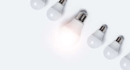 Close-up of light bulbs with one glowing against white background.