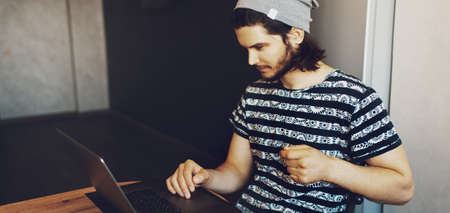 Side portrait of young handsome man working home on laptop. Panoramic banner view.