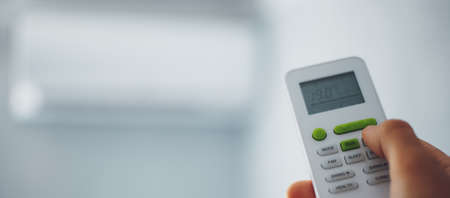 Close-up of male hand using remote control of split air conditioner. Panoramic banner with copy...