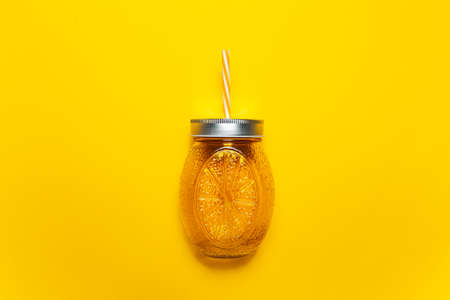 Close-up of orange juice glass mug with straw on yellow background.の写真素材
