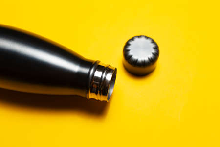 Close-up of opened, reusable steel thermo water bottle and cap on yellow background.の写真素材