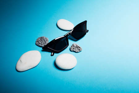 Close-up of black sunglasses near white and grey stones on blue background.の写真素材