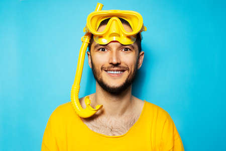 Portrait of young happy man in yellow, wearing diving mask and snorkel on blue background.の写真素材