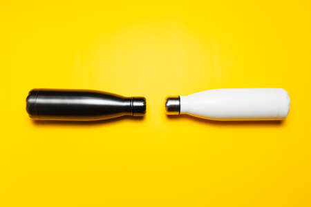 Two reusable steel thermo water bottles of white and black on yellow background.