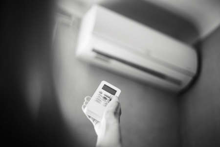 Black and white photo of hand adjusting air conditioner with remote control.の写真素材
