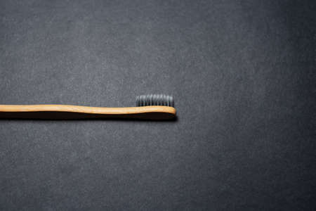 Close-up of bamboo toothbrush on background of black textured wall.