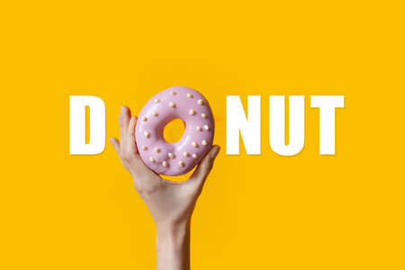 Donut text with pink donut in female hand instead of 'O' letter, on orange.の写真素材