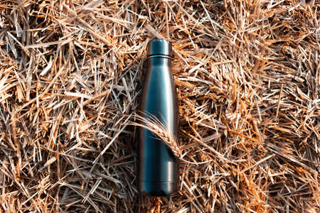 Reusable steel thermo bottle on background of dry haystack.の写真素材