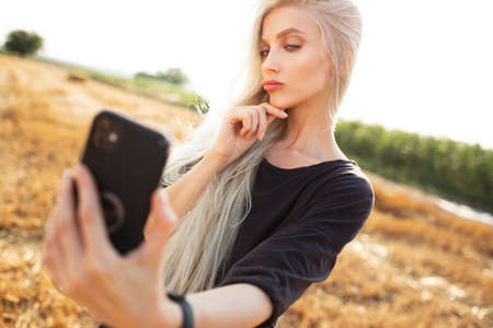 Outdoor portrait of young beauty  blonde girl, taking selfie with smartphone.