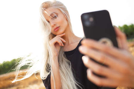 Outdoor portrait of young cute blonde girl, taking selfie with smartphone.の写真素材