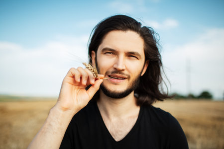 Portrait of young man with long hair holding wheat spike in mouth.の写真素材