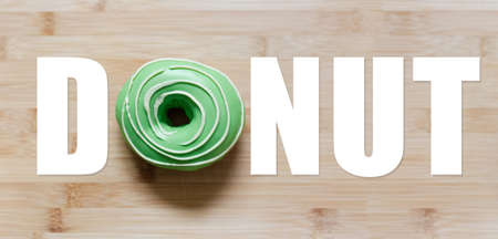 Donut word with green donut instead of 'O' letter, on wooden table.の写真素材