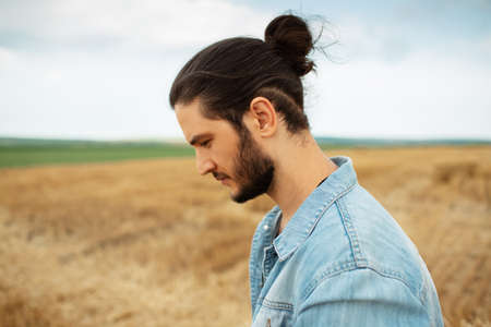 Side portrait of young hipster in denim jacket with ponytail hairstyle.の写真素材