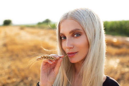 Close-up portrait of young cute blonde girl with wheat spike in mouth.の写真素材