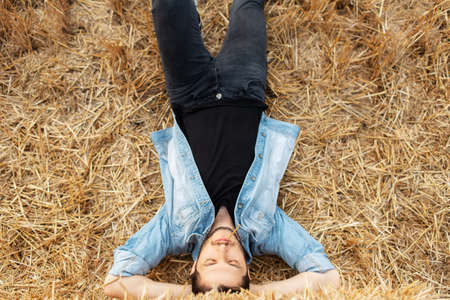 Top view of young guy in denim jacket lying on dry hay in the field.