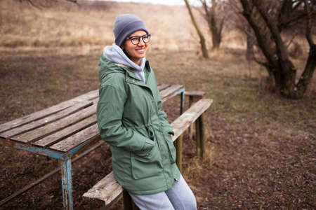 Outdoor portrait of young smiling woman, in green trench and grey hat.