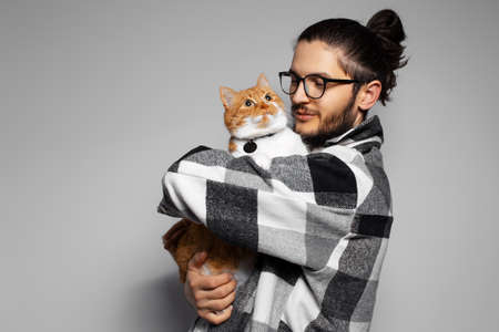 Portrait of young man holding in arms a cute red-white cat on grey background.の写真素材