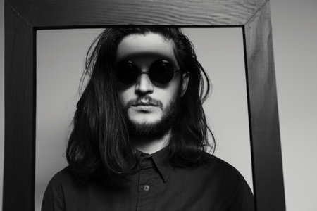 Close-up portrait of young serious man with long hair behind the black frame.の写真素材