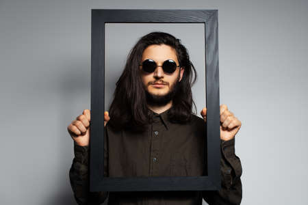 Studio portrait of young man holding empty picture frame of black.の写真素材
