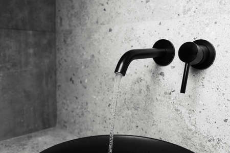 Picture of bathroom details: black washbasin and mounted tap with flowing water.