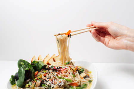 Studio photo of female hand holding chopsticks with noodles in asian ramen soup.