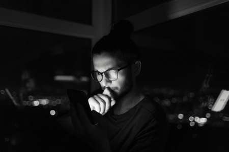 Black and white dark portrait of young man looking in smartphone.の写真素材