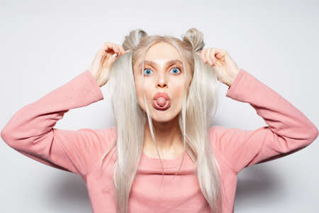 Portrait of pretty blonde girl with buns, having fun, showing tongue on white.の写真素材
