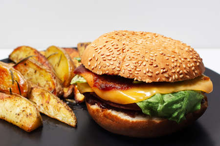 Vegan food. Close-up of homemade cheeseburger and baked potatoes on black plate.の写真素材