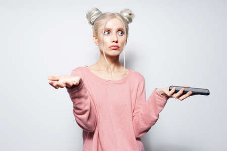 Portrait of pretty blonde girl with smartphone in hand doesn't know what to do.