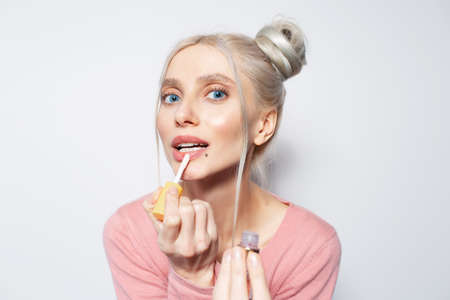 Close-up portrait of beautiful girl putting on lip gloss, on white background.の写真素材