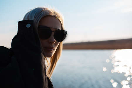 Close-up portrait of cute blonde girl wearing sunglasses near river.の写真素材