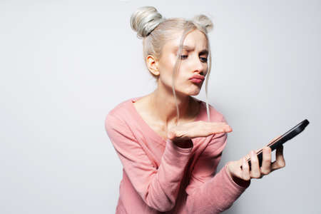Studio portrait of young blonde girl looking smartphone on white background.