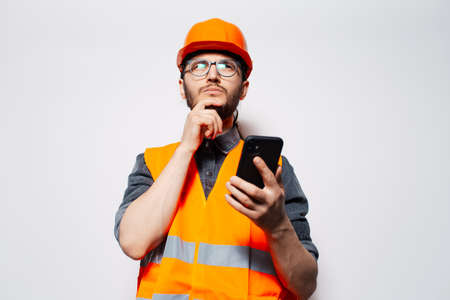 Studio portrait of young thoughtful construction worker using smartphone.