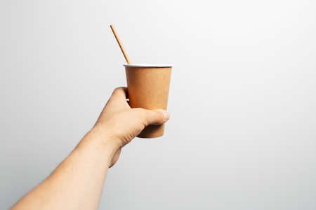 Close-up of male hand holding paper cup of coffee with bamboo straw on white.の写真素材