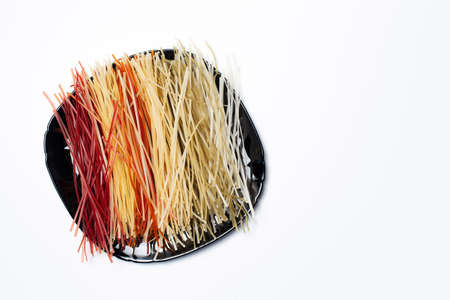 Top view of raw pasta with different colors on plate, on white with copy space.の写真素材
