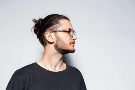 Side portrait of young guy with hair bun wearing eyeglasses on grey background.の写真素材