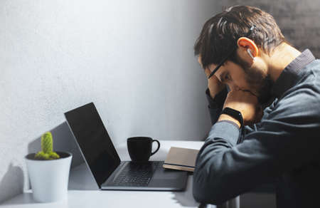 Side portrait of young sad man working online at home, looking down.の写真素材