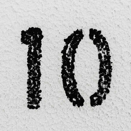Close-up of black painted number of 10 on background of grey textured wall.