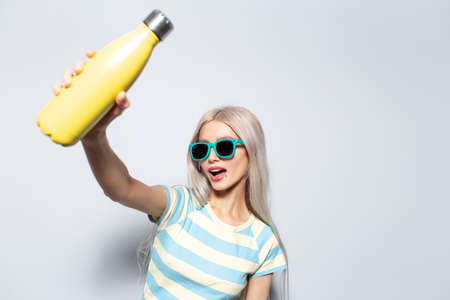 Portrait of pretty girl holding yellow thermo water bottle on white background.の写真素材