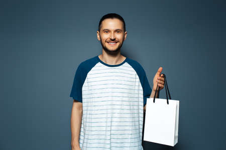 Studio portrait of young smiling man, holding a white reusable bag.
