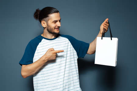 Studio portrait of young smiling man, pointing to the white bag. Empty space.の写真素材