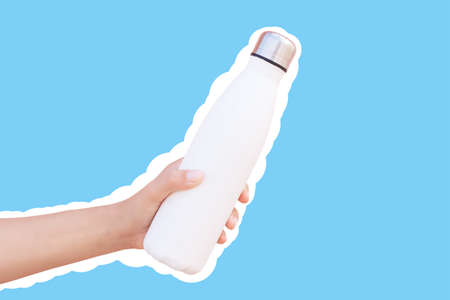Reusable thermo water bottle in hand, isolated with white contour on blue.の写真素材