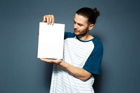 Studio portrait of guy holding white empty paper board on background of blue color.の写真素材