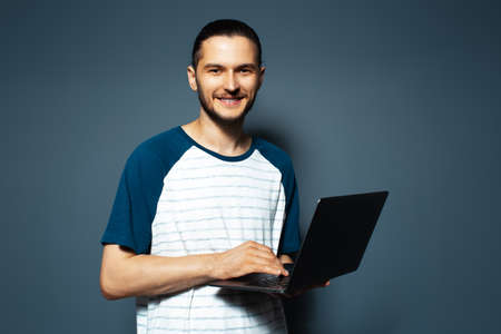 Studio portrait of guy holding opened laptop, on blue background.