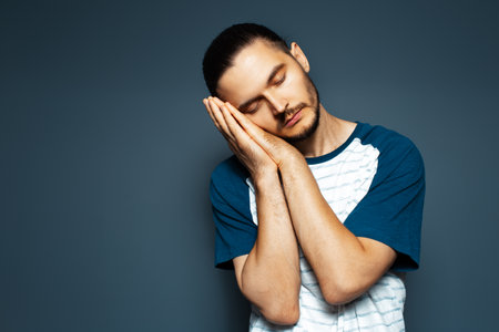 Studio portrait of guy making sleeping gesture on blue background.の写真素材
