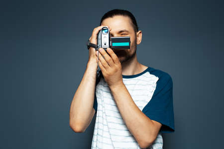 Studio portrait of young guy with digital video camera in hands. Making movie.の写真素材