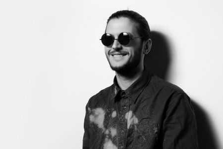 Black and white studio portrait of young smiling man, wearing sunglasses.
