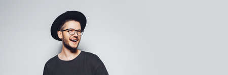 Studio portrait of young happiness man wearing eyeglasses and black hat on grey background with copy space. Panoramic banner view.の写真素材