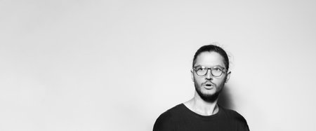 Studio portrait of young surprised man wearing eyeglasses on grey background with copy space. Panoramic banner view. Black and white photo.の写真素材